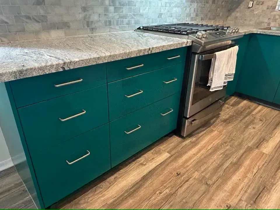 Teal kitchen cabinets with granite countertop and a stainless steel stove. Wooden floor.