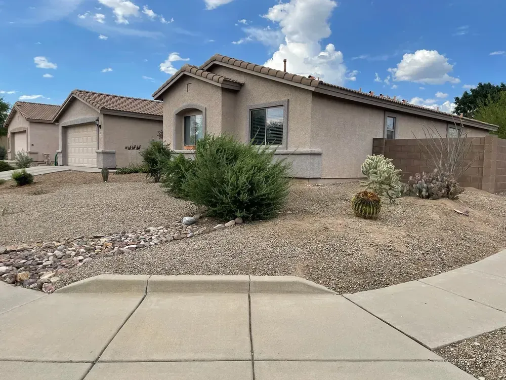 Beige house with a gravel yard, blue sky, and a sidewalk in front.