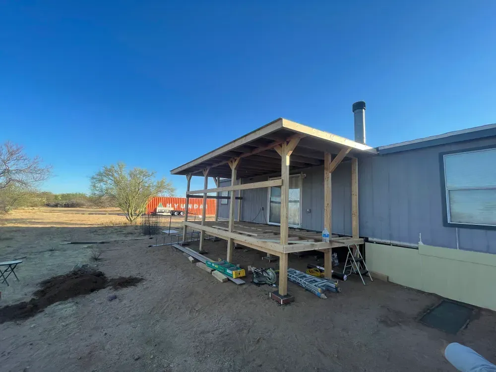 A porch under construction is attached to a blue house on a sunny day.