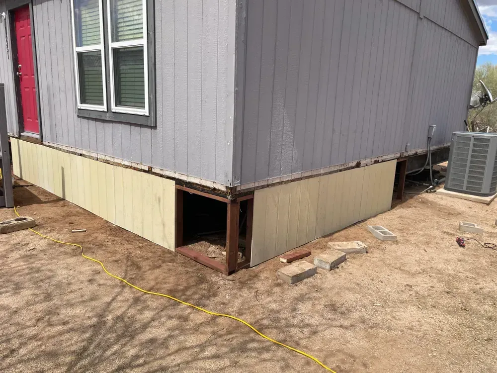 Gray and tan building with exposed foundation, red door, and AC unit outside.