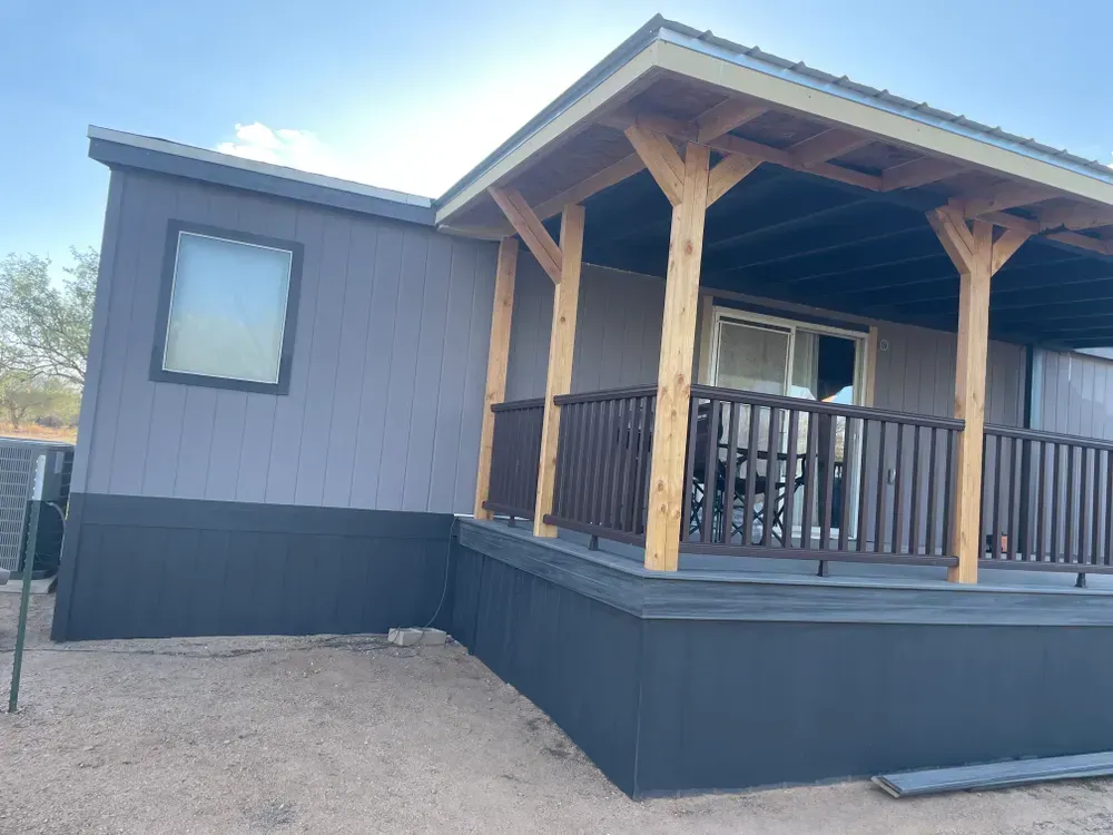 Exterior view of a gray house with a wooden porch, sliding glass door, and dark blue siding.