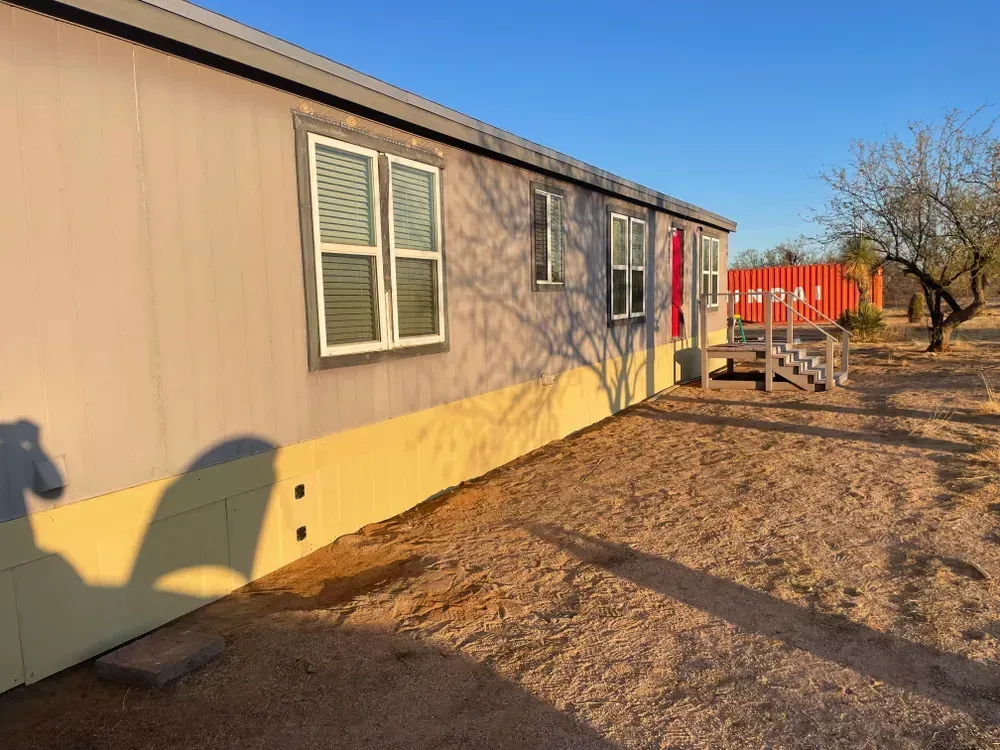 Side view of a beige mobile home with red door, set in a desert landscape.