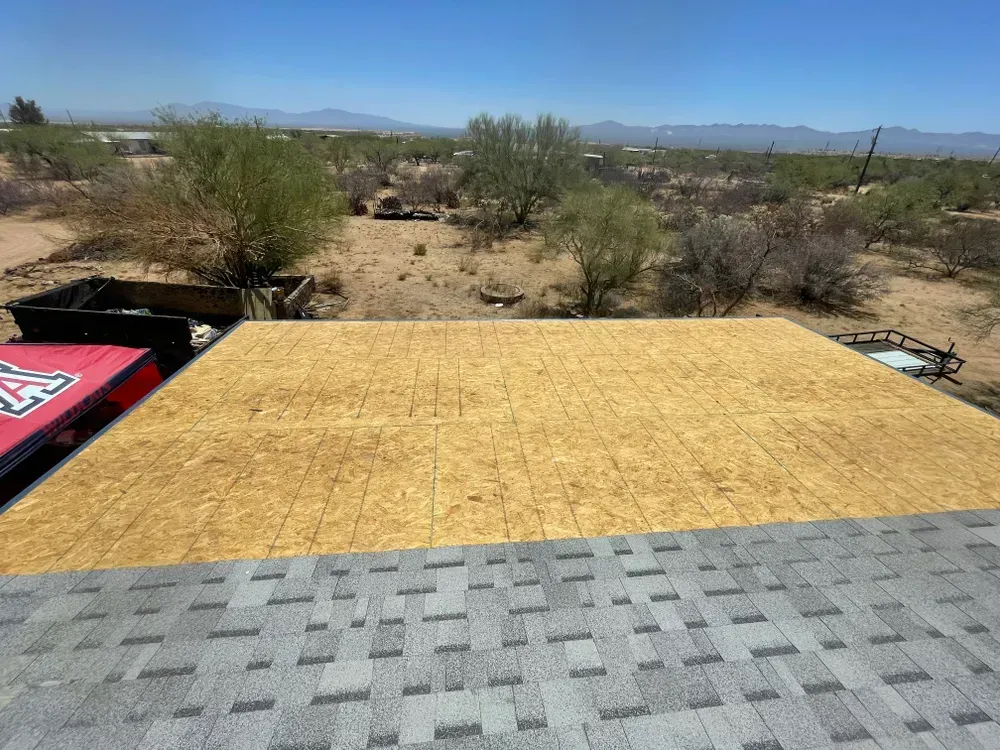 A roof with grey shingles in foreground, with new OSB sheathing. Desert landscape in background.