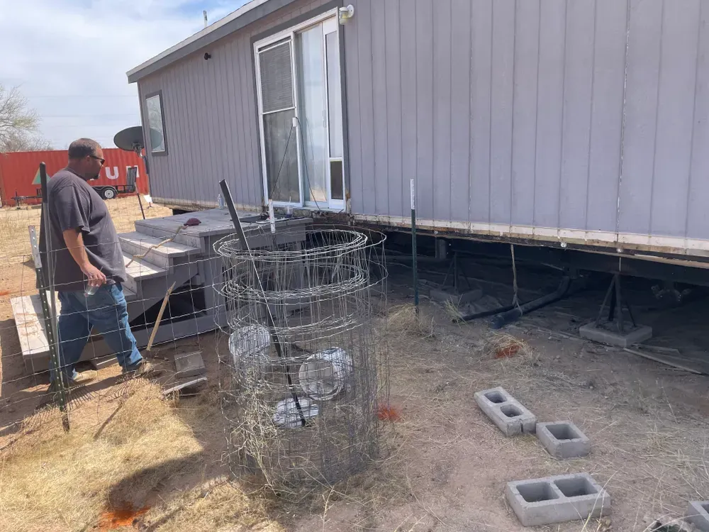 Man near a house with stacked cinder blocks and a wire structure in a yard.