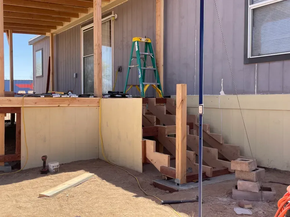 Construction of wooden steps and deck attached to a house with blue siding.
