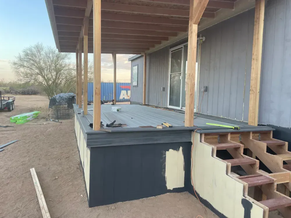 Construction of a deck with a covered porch on a house exterior. Gray siding, wooden supports, and steps.