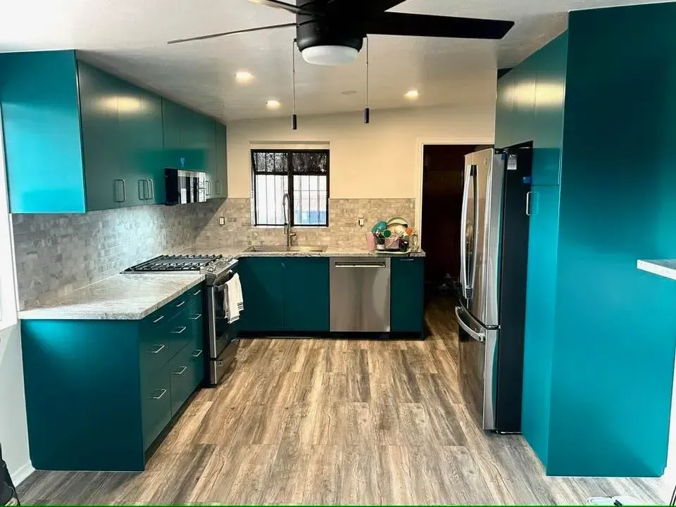 Teal kitchen with cabinets, stainless steel appliances, speckled countertops, and wood-look flooring.