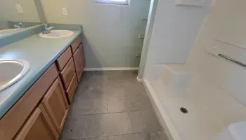 Bathroom with dual sinks, wooden cabinets, gray tile floor, and a shower stall.