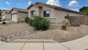 Tan stucco house with gravel yard, shrubs, and a cloudy blue sky.