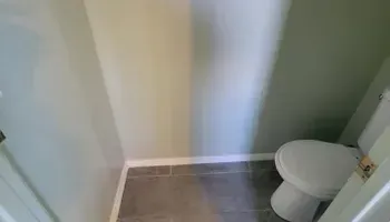 Small bathroom with a toilet. Green and cream colored walls and gray tile floor.