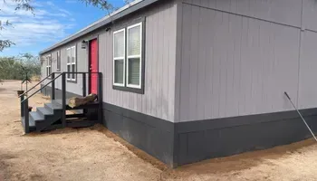 Gray mobile home with dark trim, red door, and steps leading to the entrance.