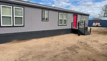 Gray mobile home with black trim, a red door, and a container in the background.
