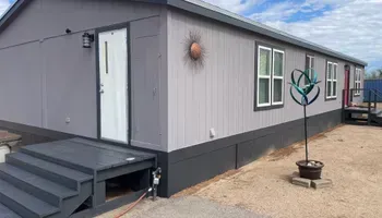 Gray mobile home with dark gray trim, front door, and steps. Decorative sun and sculpture in front.