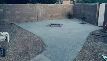Backyard patio with gravel, concrete pavers, and a fire pit, surrounded by a cinder block wall.