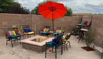 Patio with fire pit, seating, orange umbrella, and brick walls.