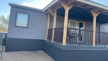 Gray house with porch, brown beams and railing. Dark gray trim. Small window.