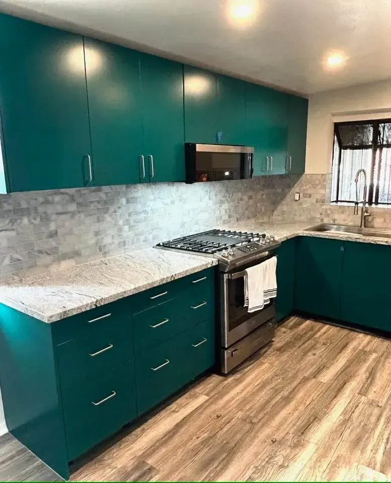 Teal kitchen cabinets with a stainless steel stove, gray countertops, and light wood-look flooring.