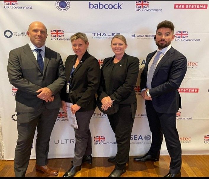 Four people in suits stand for a group photo against a branded backdrop.