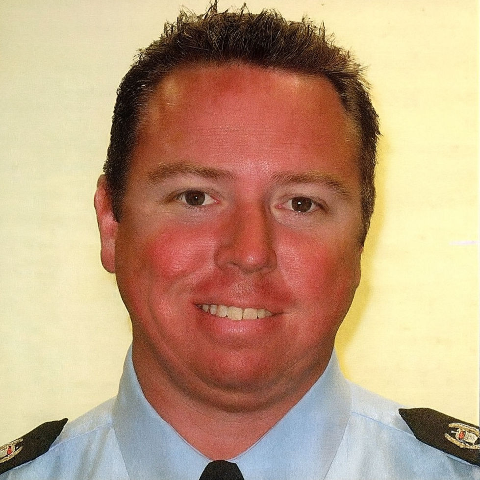 Man in light blue uniform with black tie, smiling.