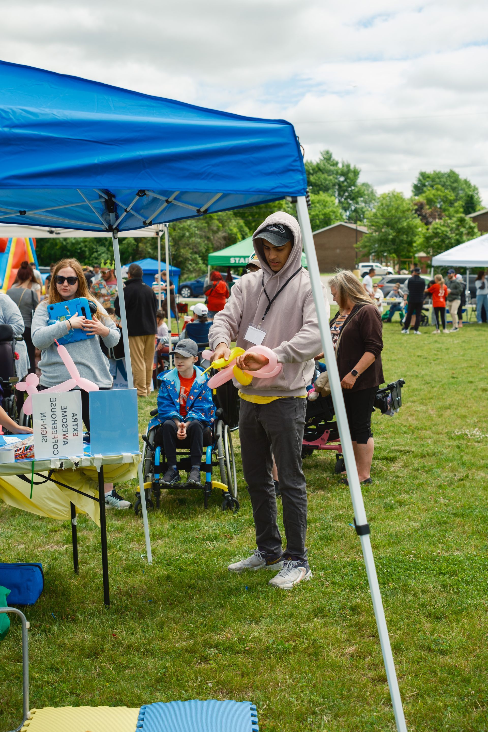 A man is standing under a blue tent in a field holding balloons.