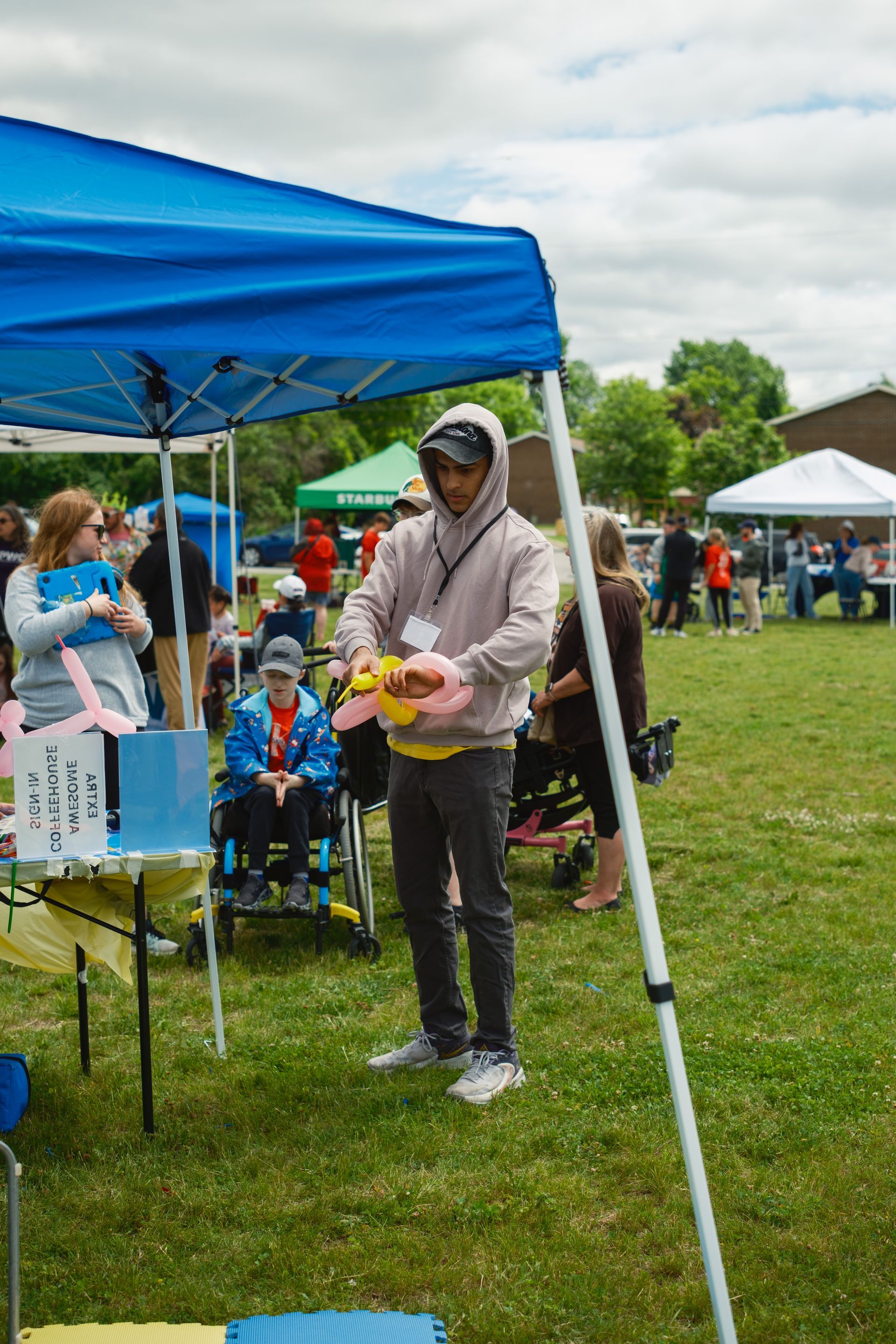 A man is standing under a blue tent in a field holding a balloon.