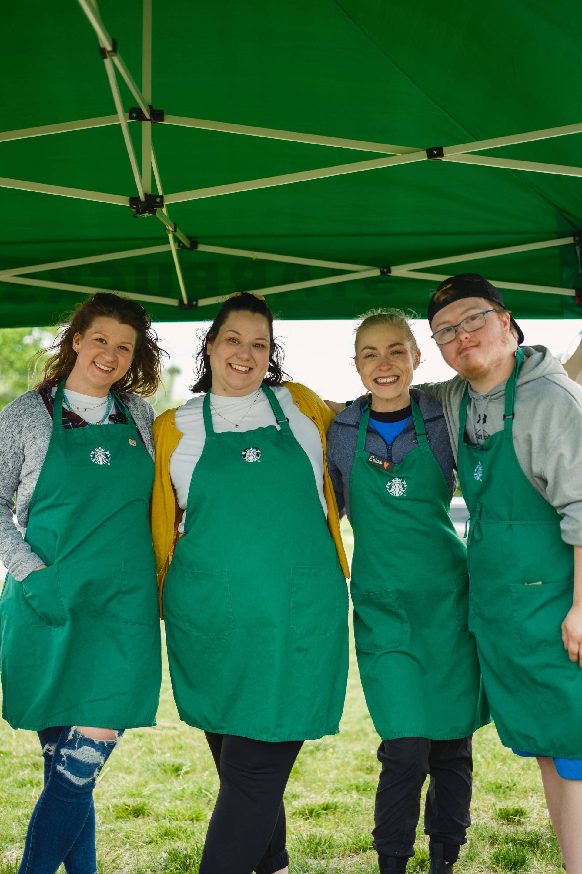 A group of people wearing green aprons are posing for a picture under a green tent.