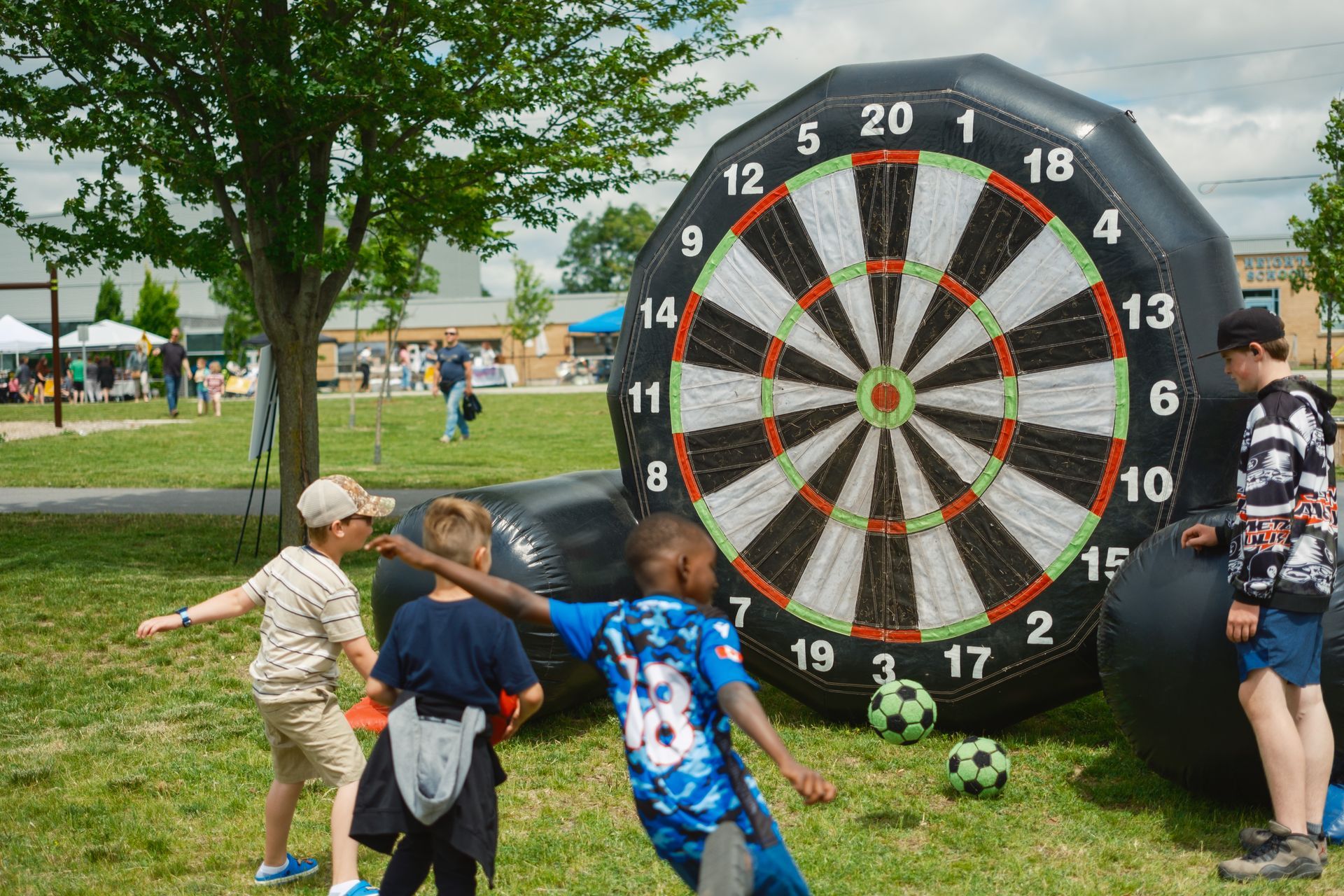 A group of children are playing soccer in front of an inflatable dart board.