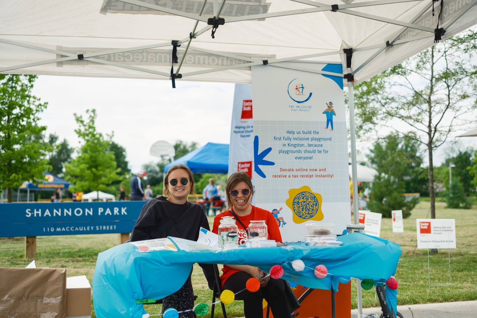 Two people are sitting at a table under a tent in shannon park.