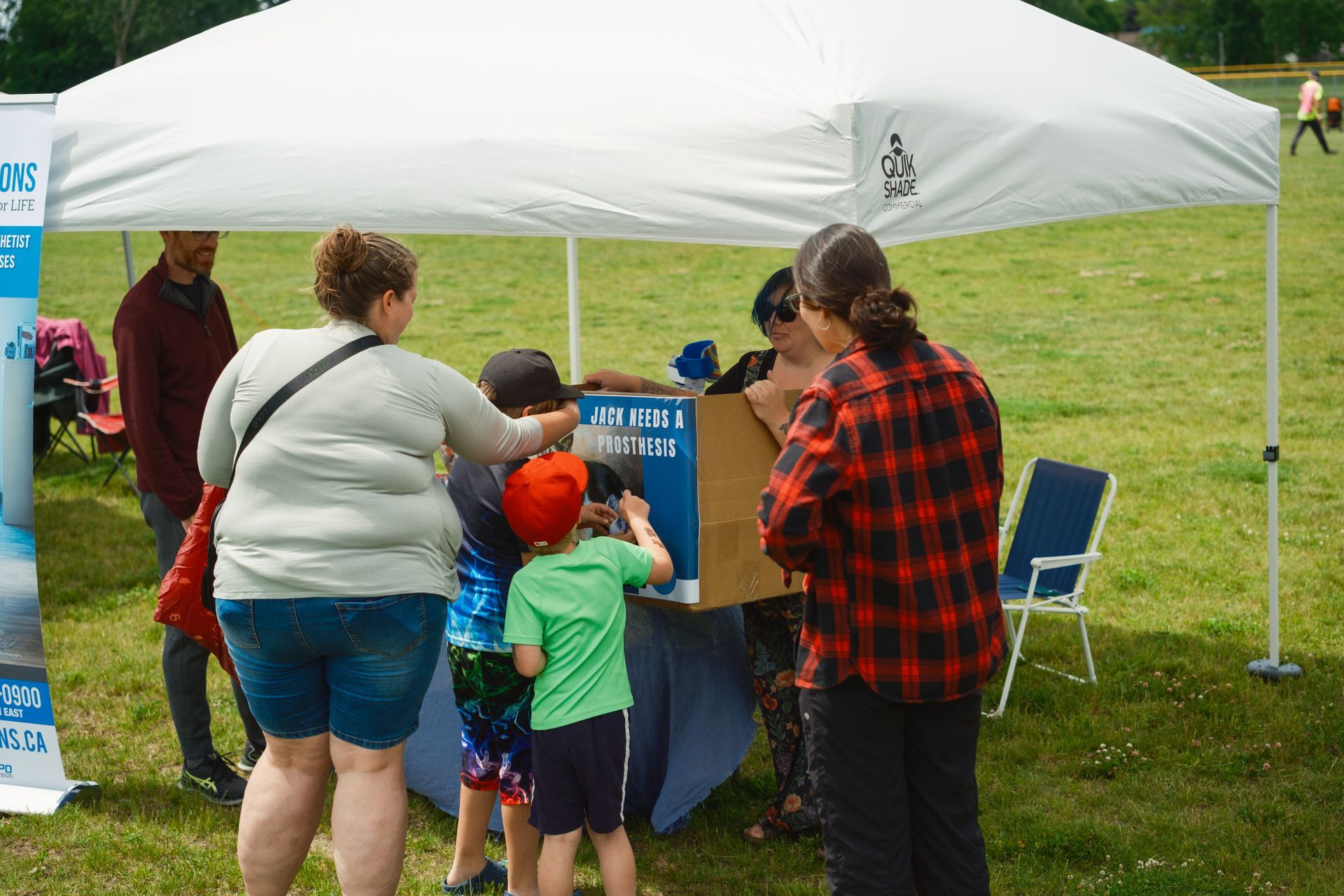 A group of people are standing around a table under a tent in a field.