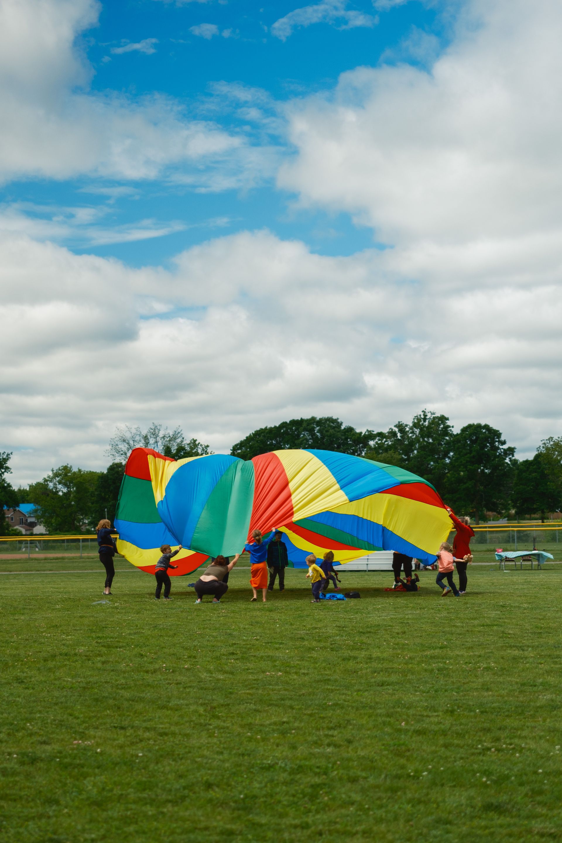 A group of people are playing with a colorful parachute in a field.