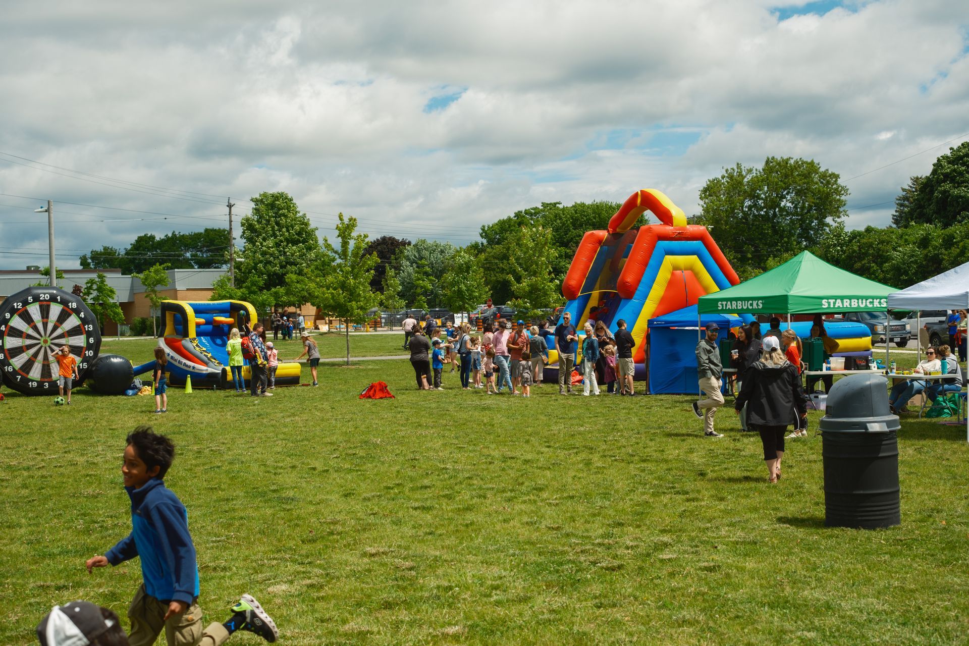 A group of people are playing in a park with a bouncy house and a dart board.