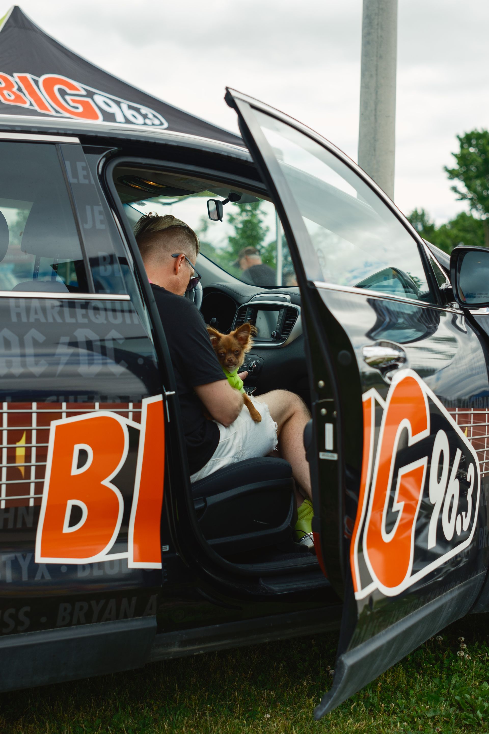 A man is sitting in the back seat of a car holding a dog.