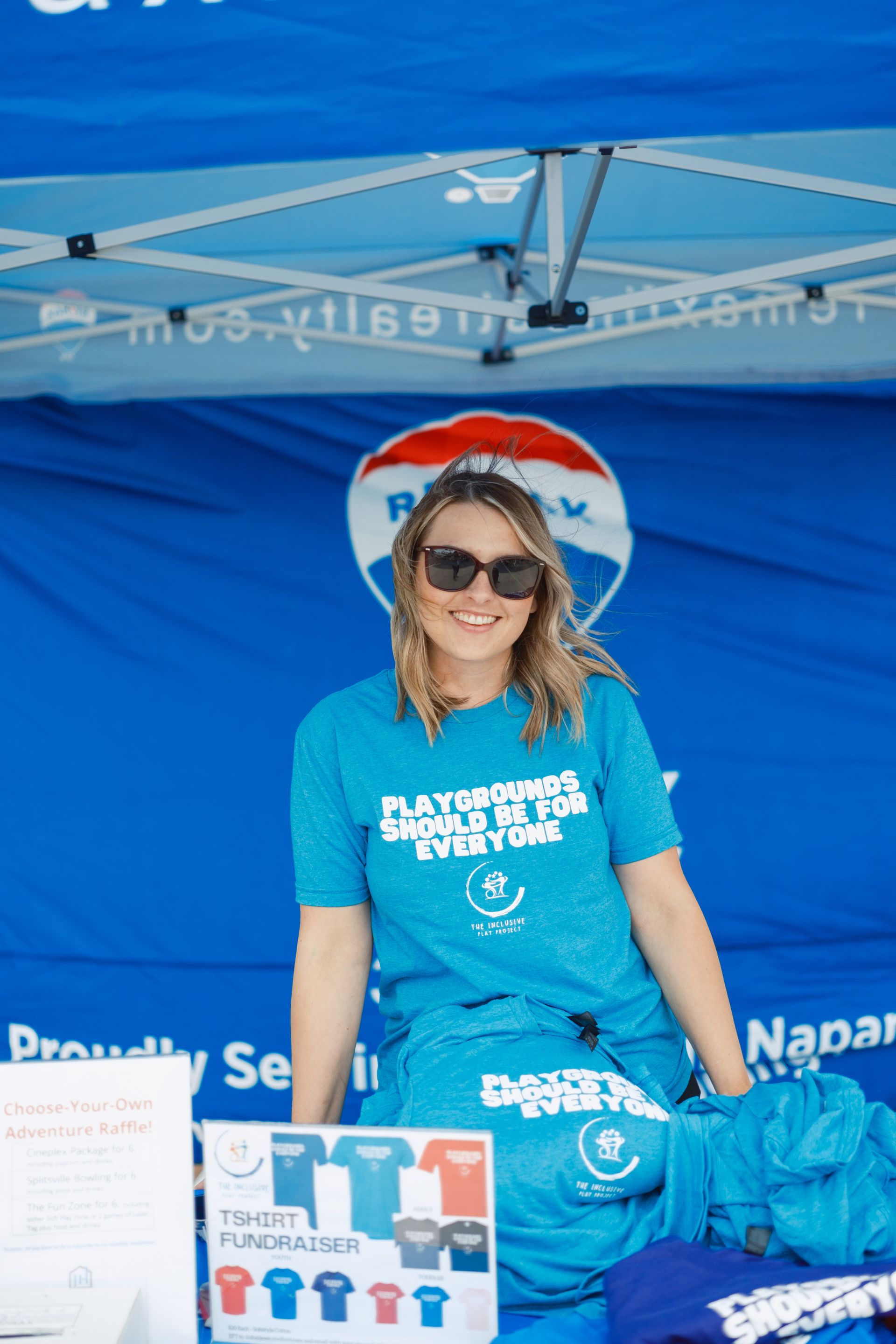 A woman in a blue shirt is standing in front of a blue tent.