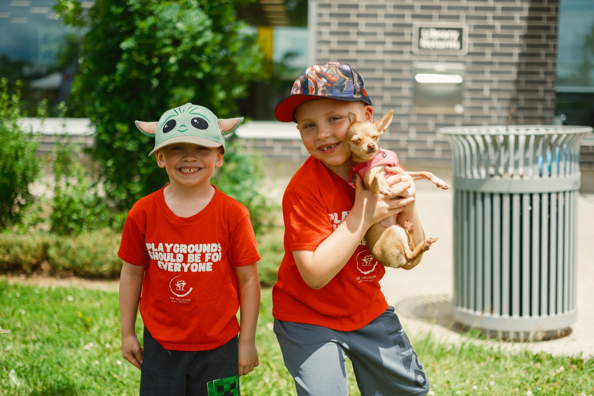 Two young boys are standing next to each other holding a small dog.