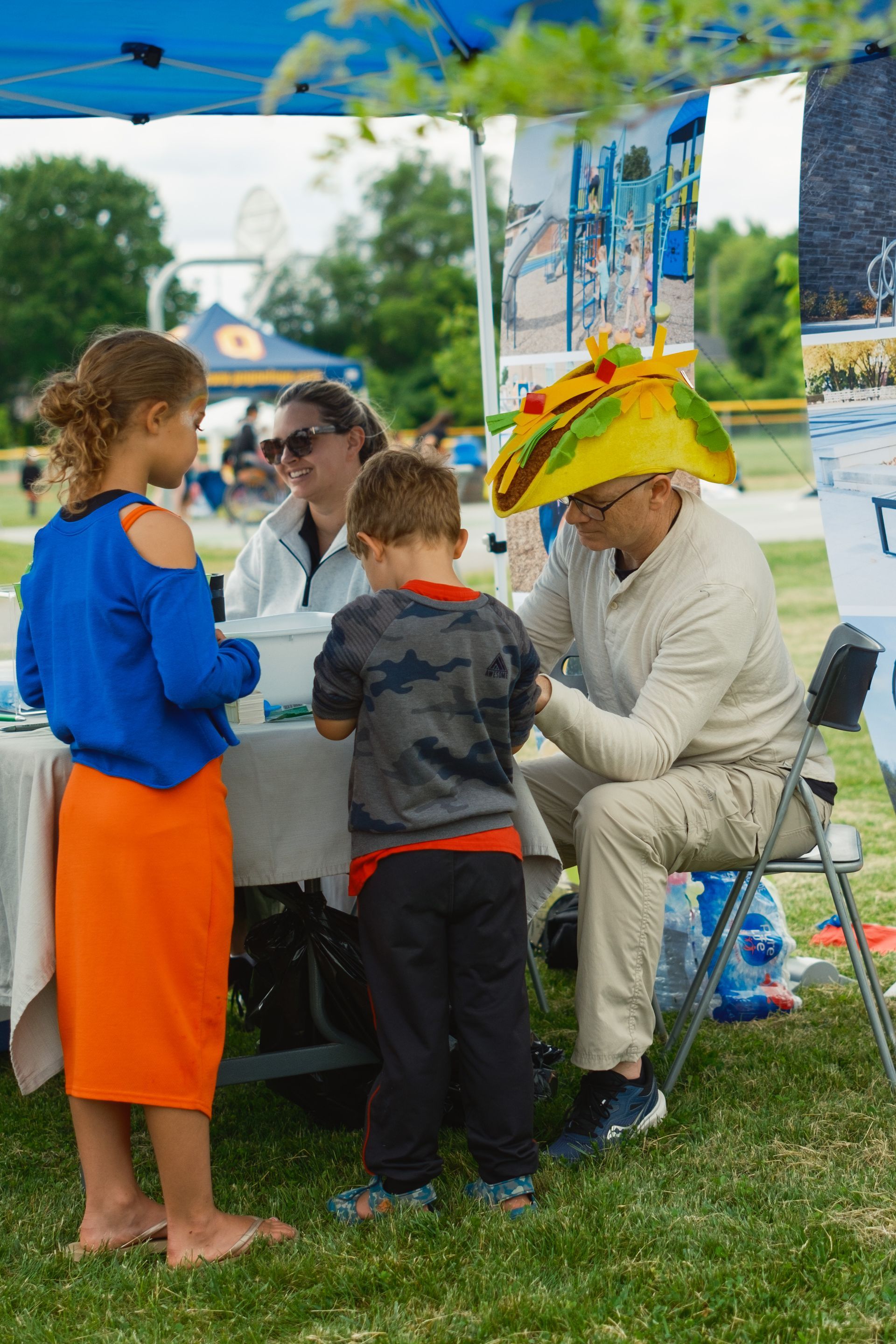 A man wearing a yellow hat is sitting at a table with two children.