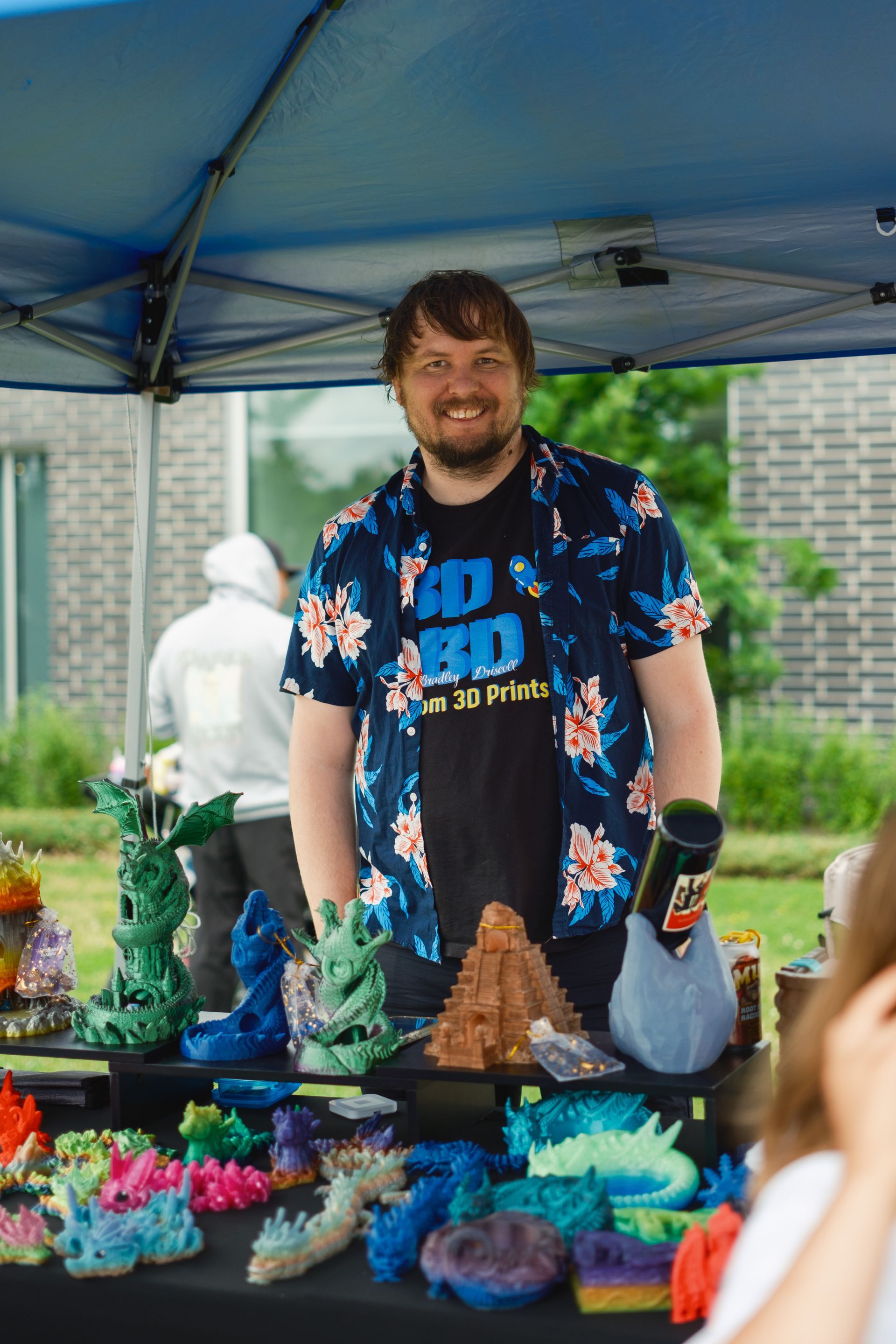 A man in a floral shirt is standing in front of a tent.