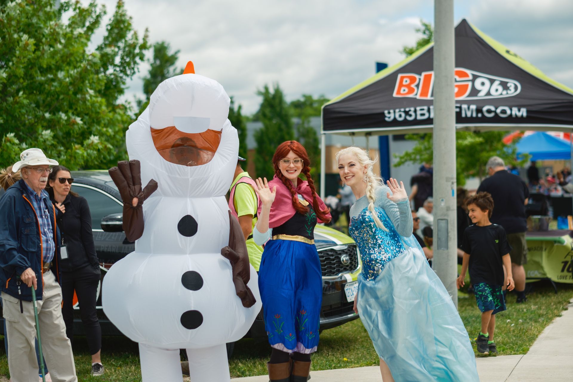 A group of people dressed as elsa and anna are standing next to a snowman.