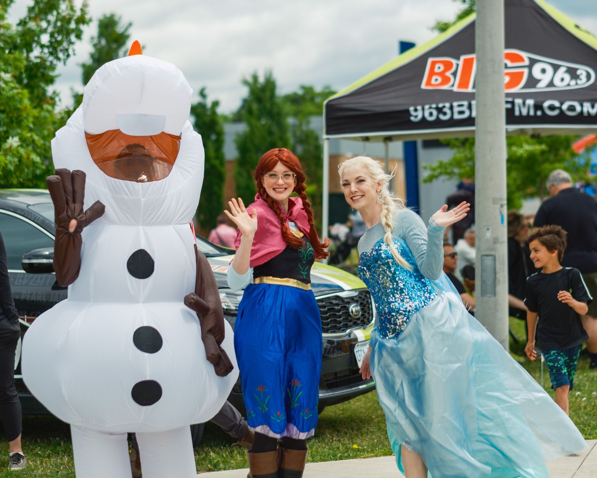 Two women dressed as anna and elsa are standing next to a snowman.