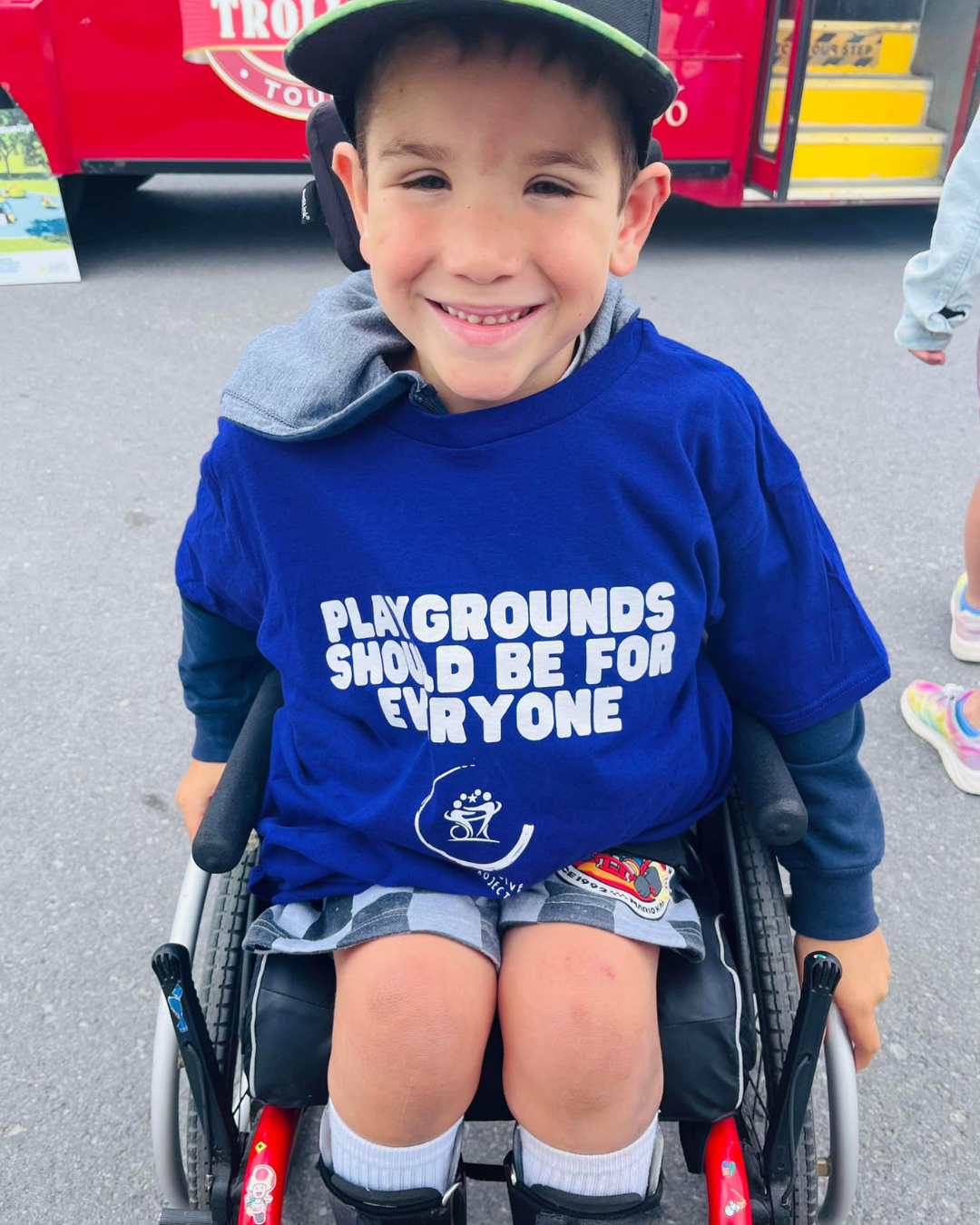 A young boy in a wheelchair wearing a shirt that says playground should be for everyone