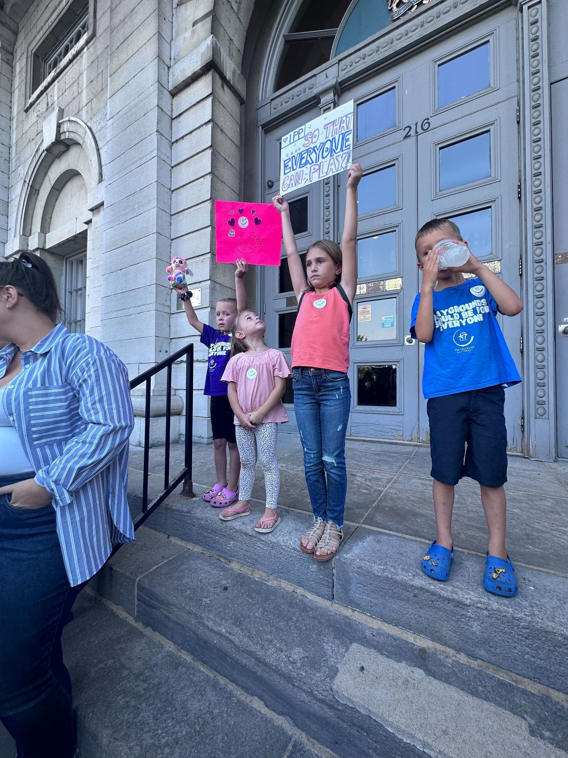 A group of children are standing in front of a building holding signs.