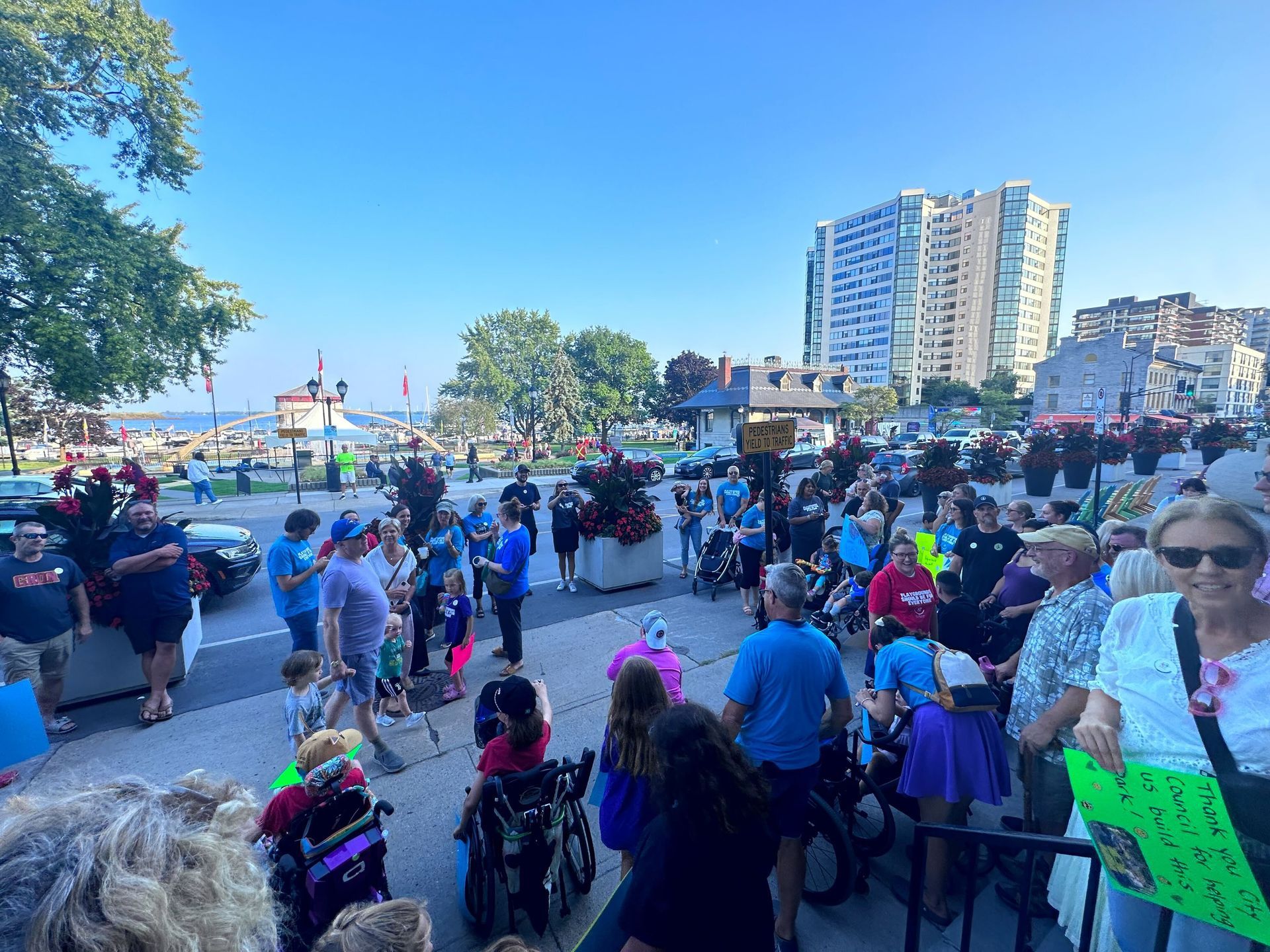 A large group of people are standing on the sidewalk holding signs.