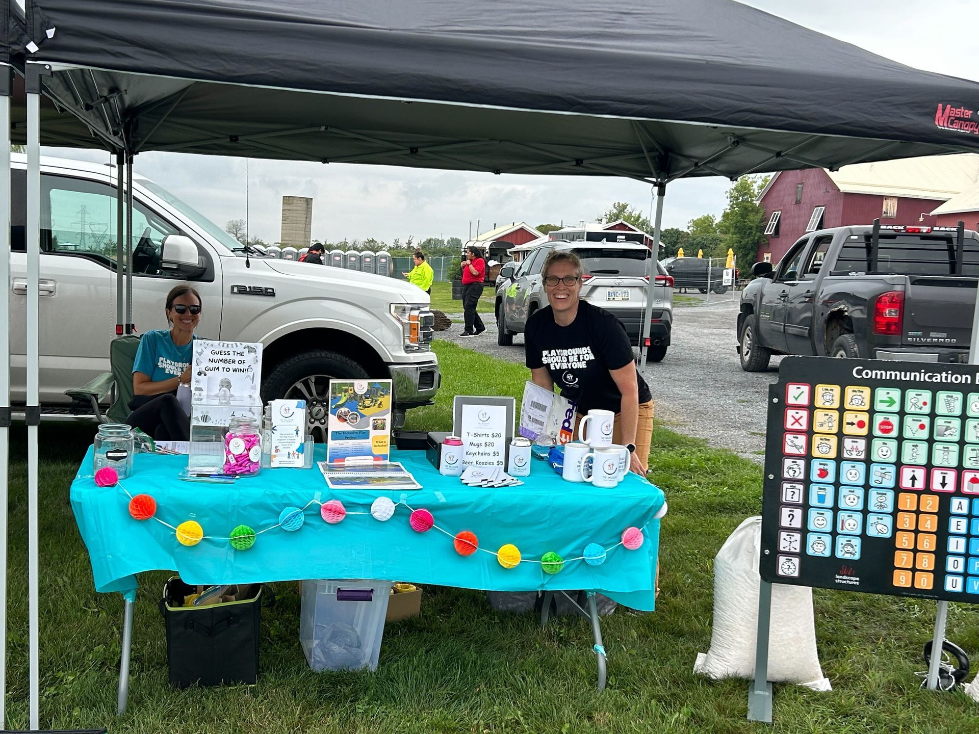 A man is sitting at a table under a tent in a parking lot.