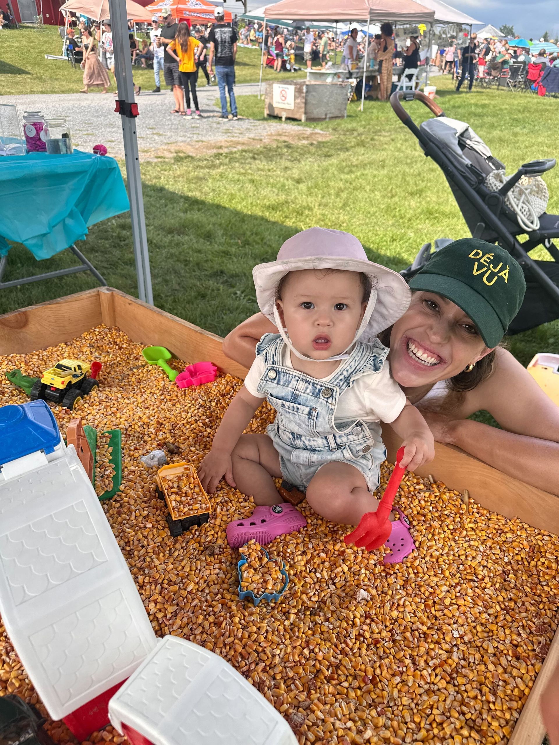 A woman and a baby are playing in a sandbox filled with corn.
