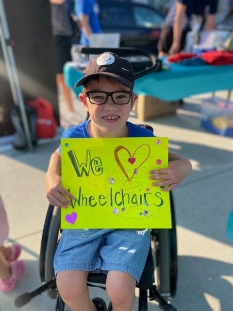 A young boy in a wheelchair is holding a sign that says we love wheelchairs