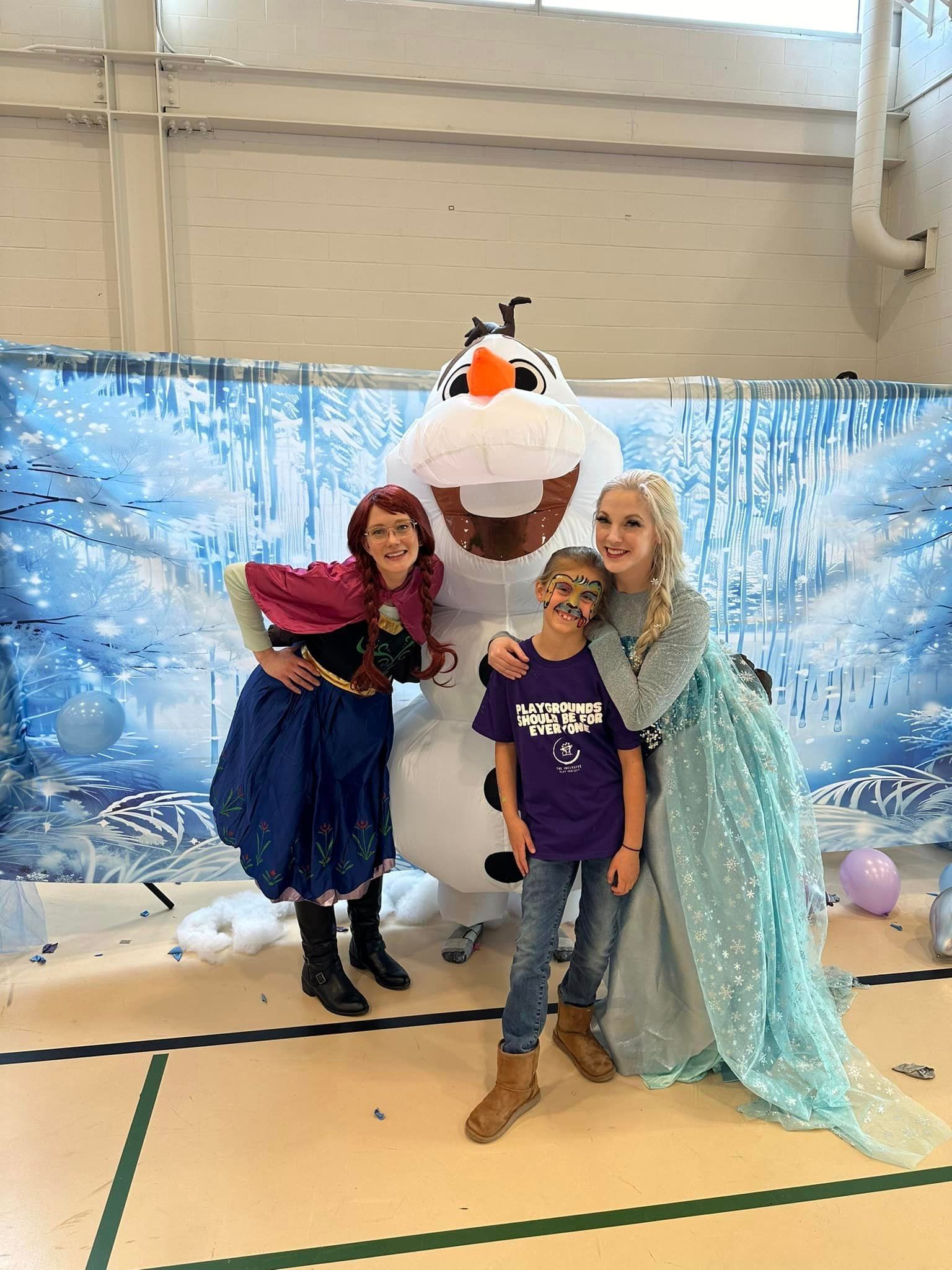 Two women dressed as anna and elsa are posing for a picture with a snowman.