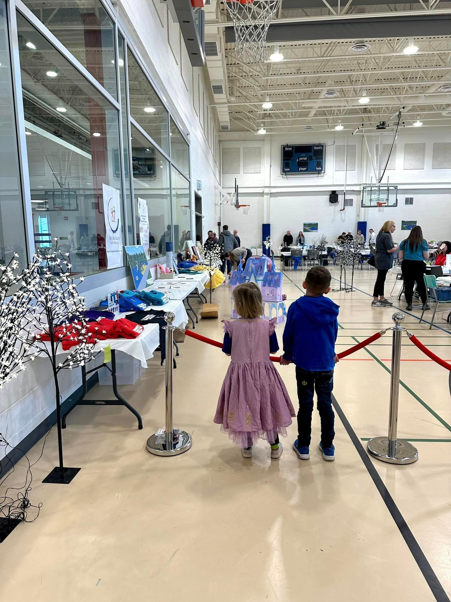 A boy and a girl are standing in a gym looking at a table.