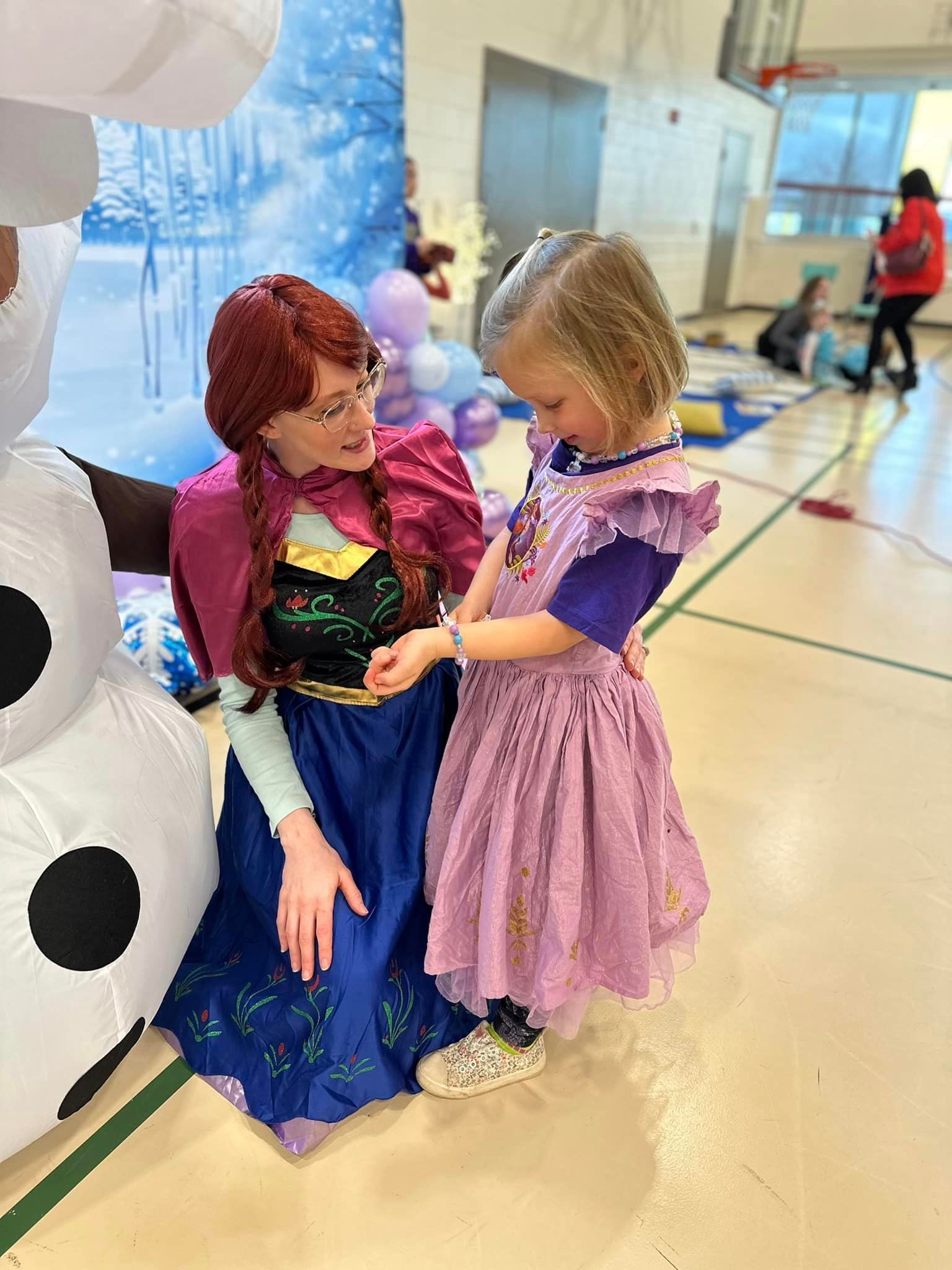 Two little girls dressed as anna and rapunzel are standing next to each other in a gym.