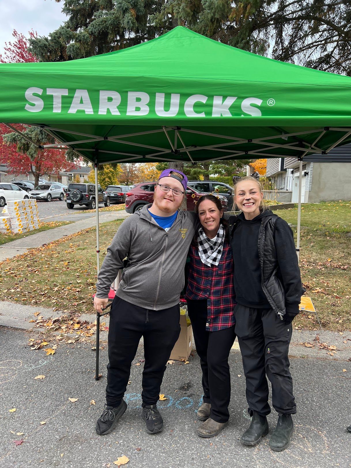 Three people are posing for a picture under a green starbucks tent.
