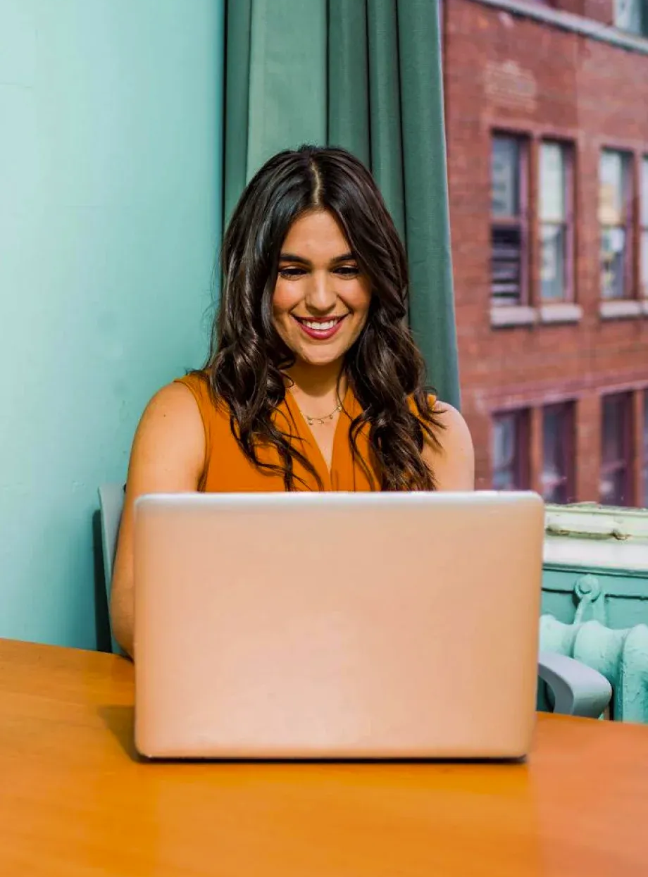 Uma mulher está sentada à mesa usando um laptop.