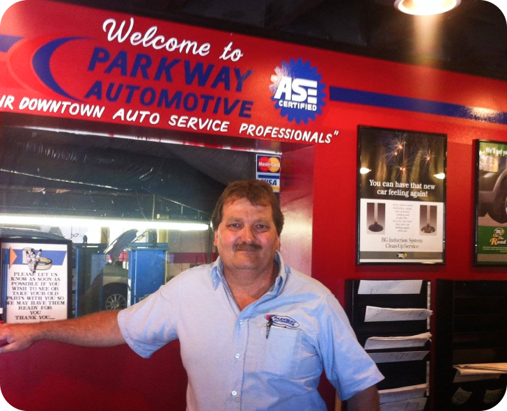 A man stands in front of a sign that says welcome to parkway automotive | Parkway Automotive